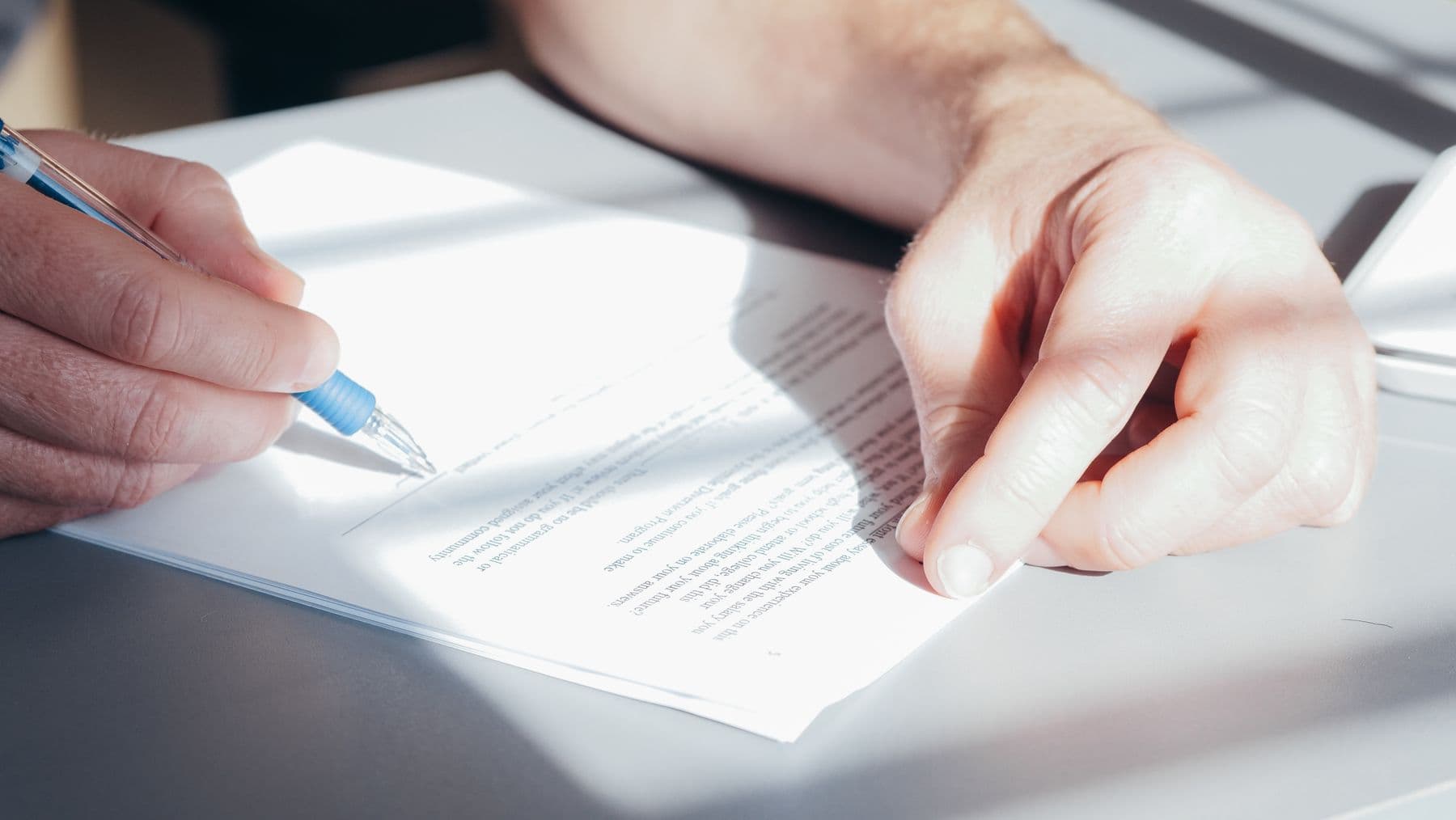 Two people signing a contract at a desk