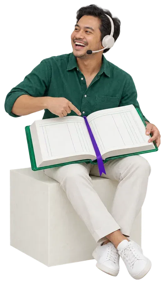 A smiling man in a headset, sitting on a block and pointing at an open ledger on his lap